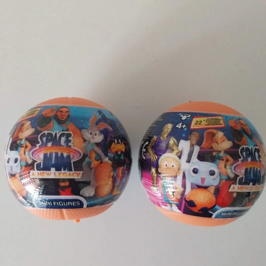 Deux sphères d'emballage colorées de mini figurines Space Jam S1, comportant des illustrations de personnages du film Space Jam. Les emballages sont de couleur bleu avec des couvercles orange et affichent des images de personnages comme Bugs Bunny et d'autres icônes du film. Chaque sphère est marquée comme un assortiment surprise, indiquant qu'elle contient deux figurines aléatoires.